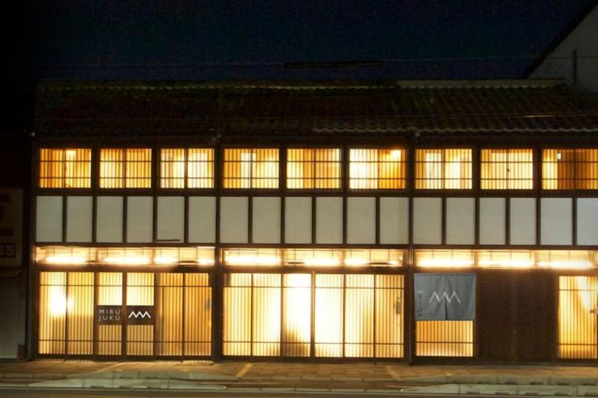 A two-story building with a traditional facade, illuminated windows, and a sign with a logo.