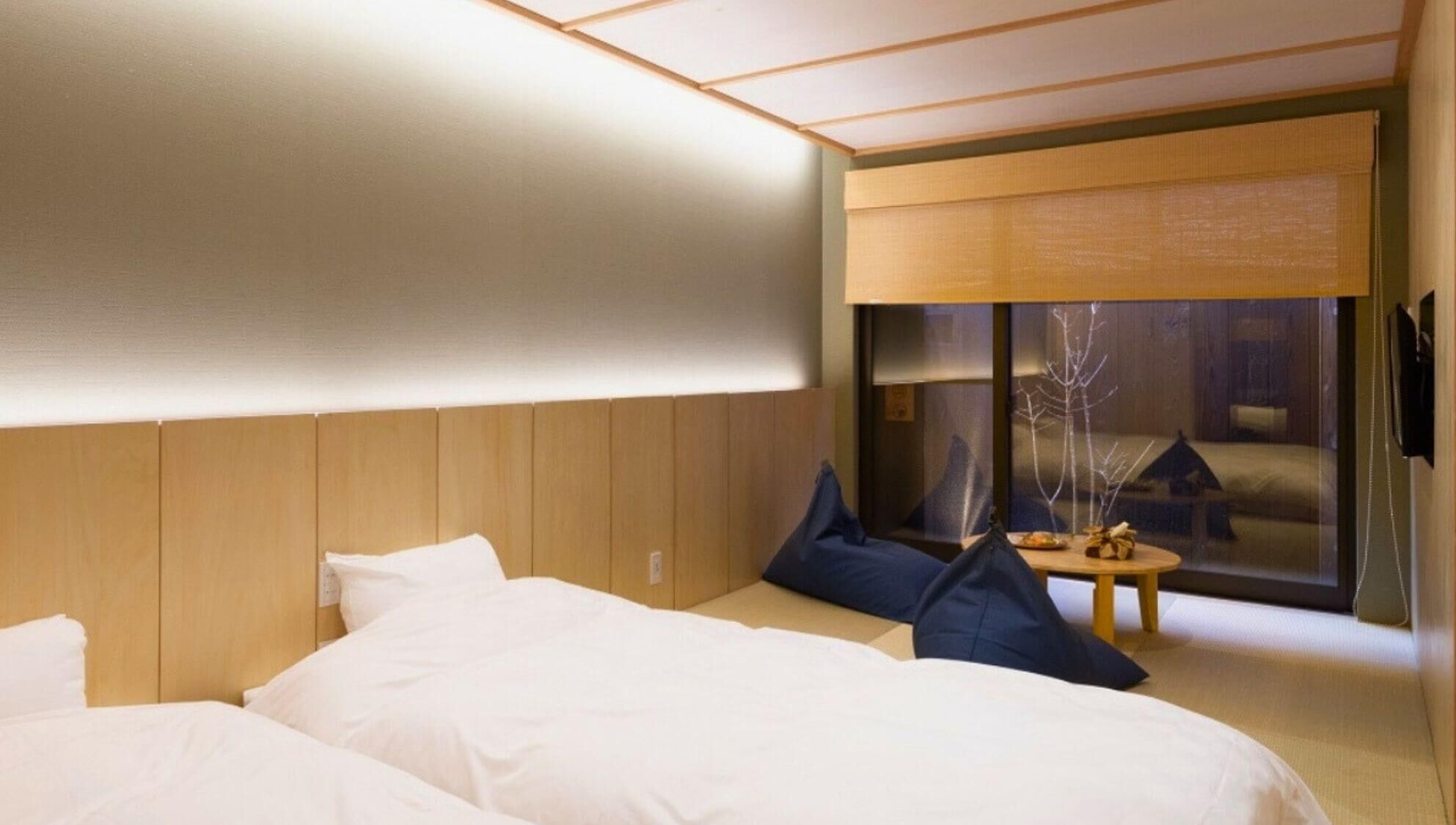 Hotellihuoneessa on suuri sänky, pienempi sänky, työpöytä ja ikkunasta avautuu näkymä rakennukseen.