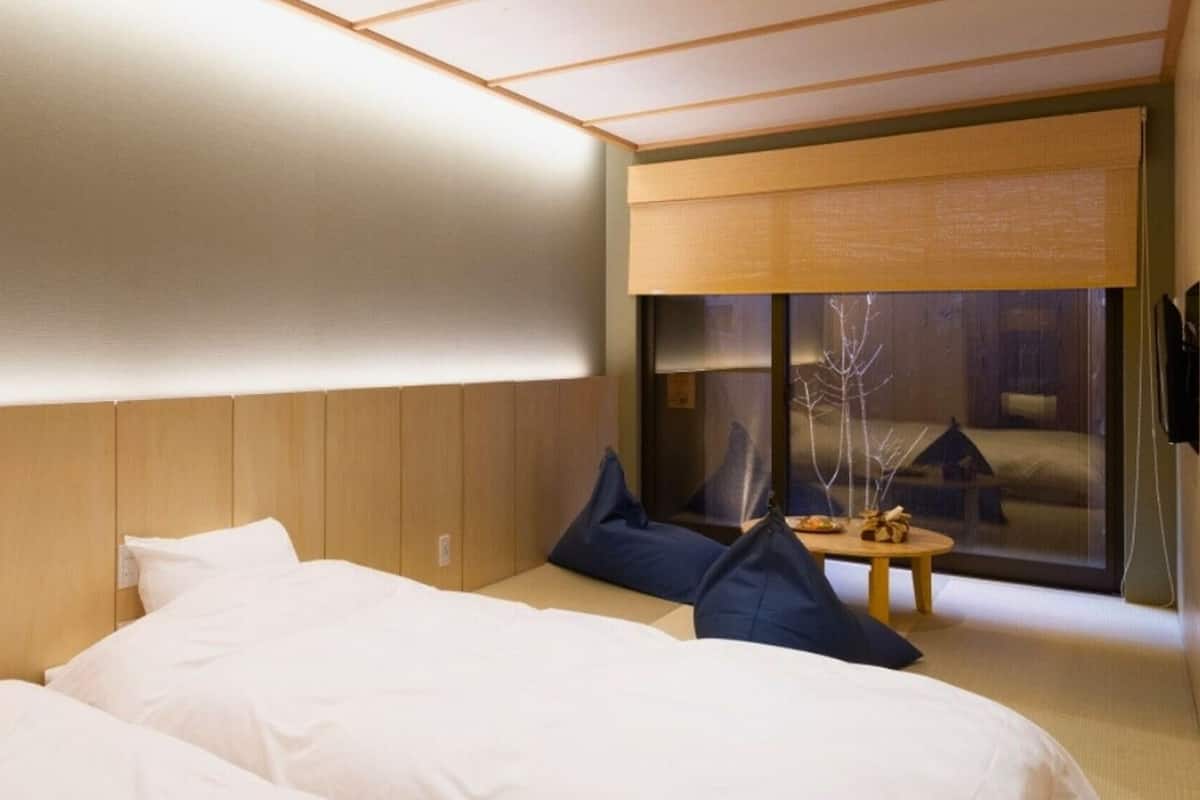 Hotellihuoneessa on suuri sänky, pienempi sänky, työpöytä ja ikkunasta avautuu näkymä rakennukseen.
