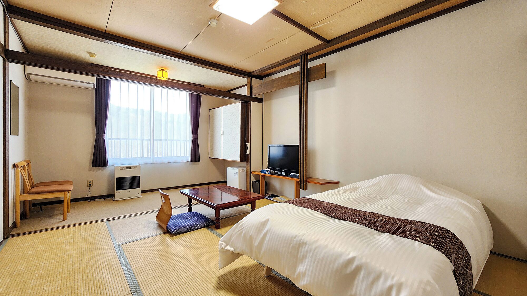 Una habitación de hotel con cama, escritorio, silla, televisión y ventana con cortinas.