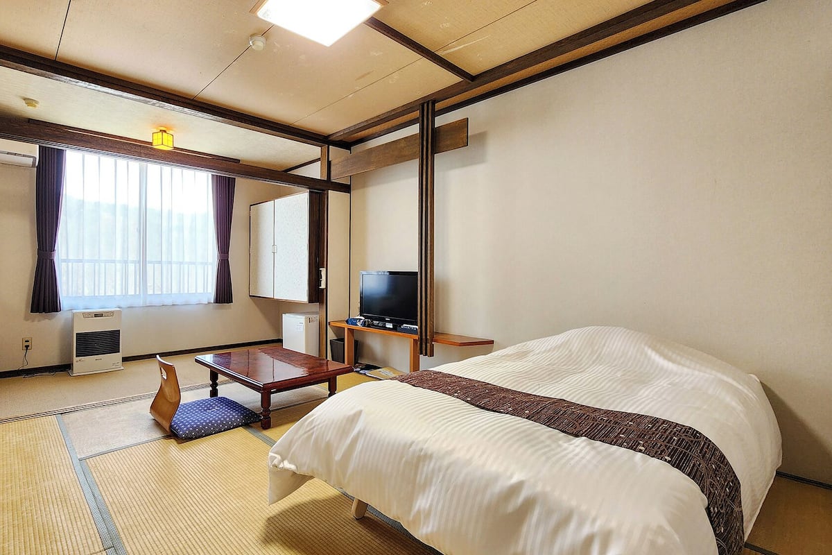 Une chambre d’hôtel équipée d’un lit, d’un bureau, d’une chaise, d’une télévision et d’une fenêtre avec des rideaux.
