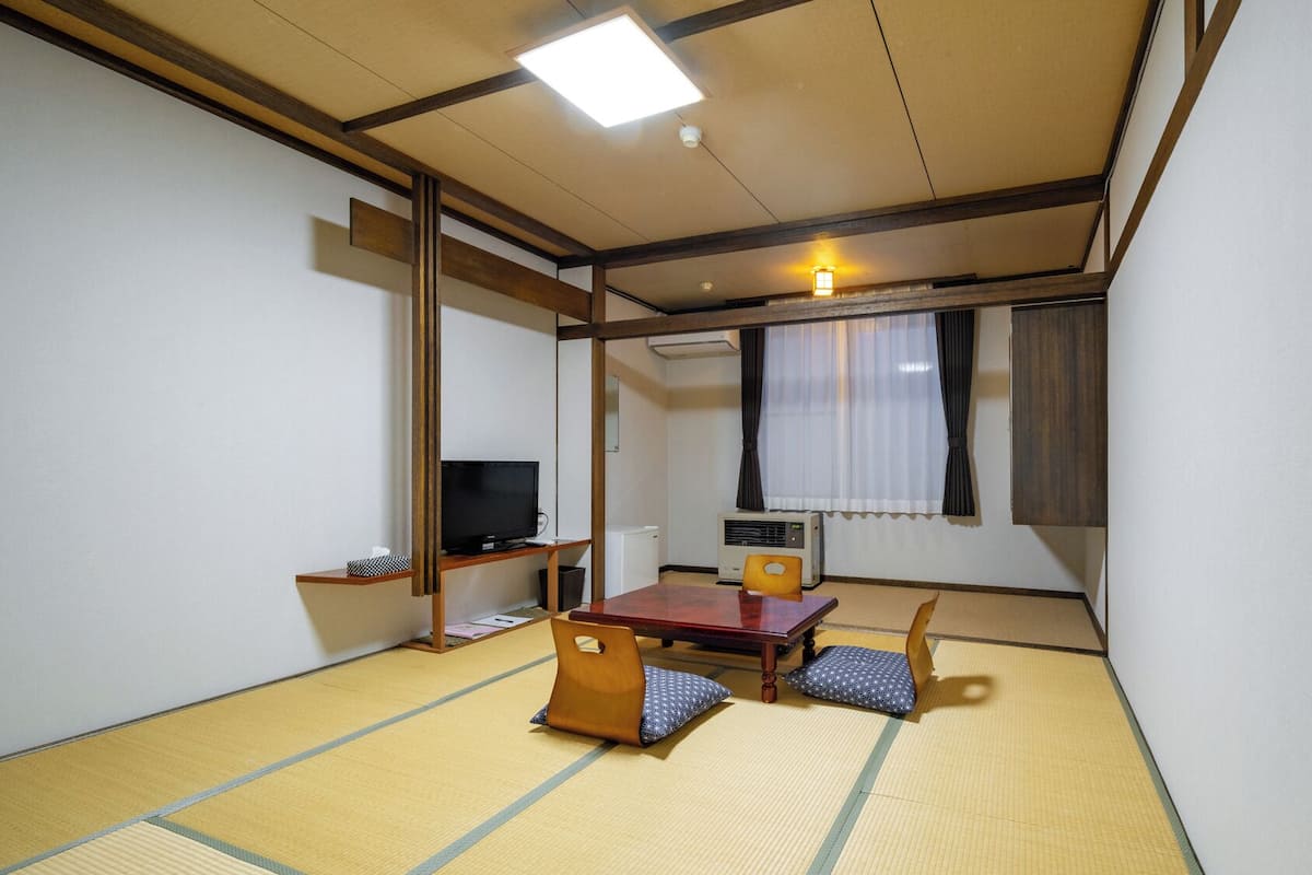 Une pièce de style japonais traditionnel, avec un sol recouvert de tatamis, une table basse, un téléviseur et un radiateur.