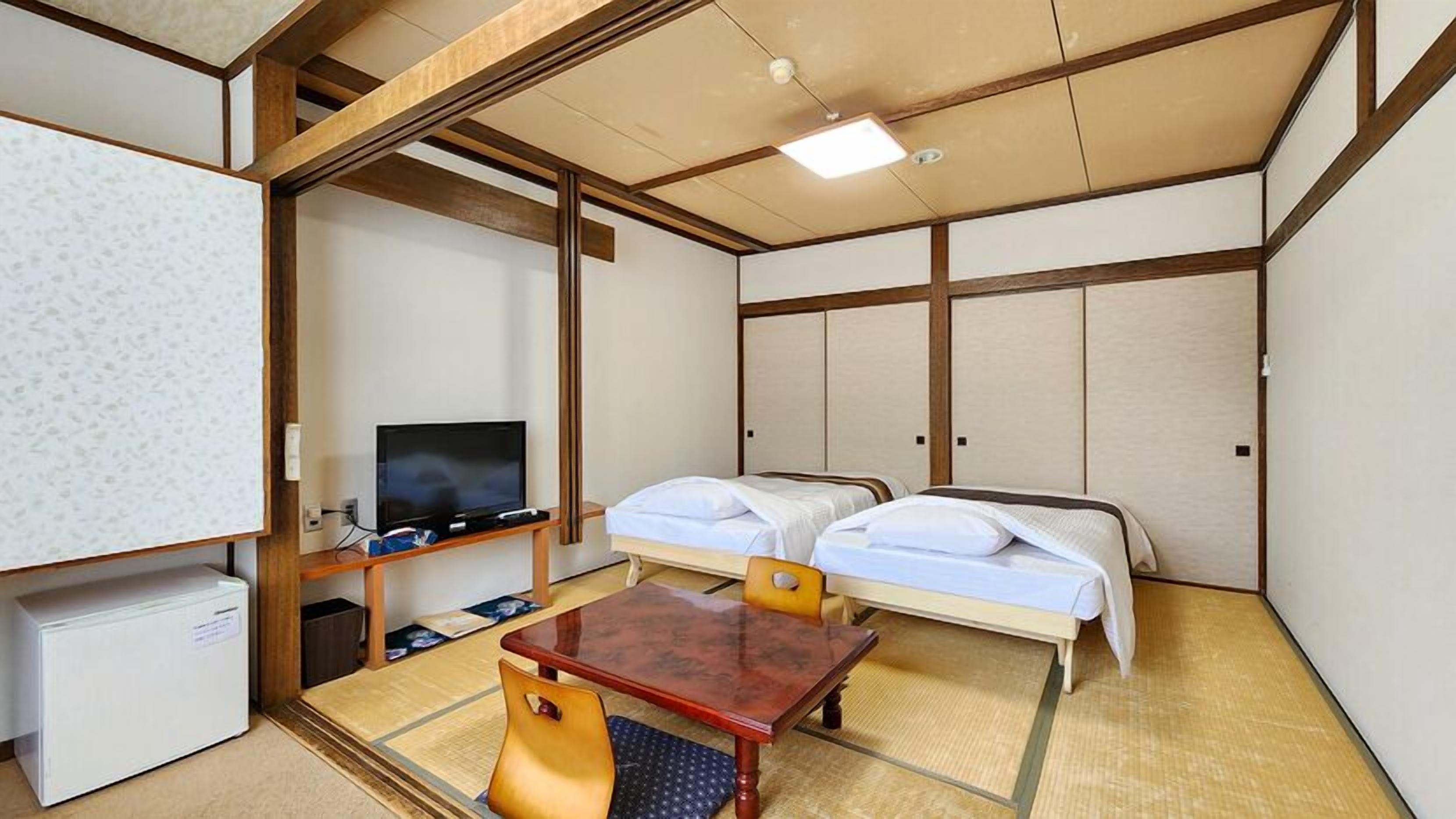 Habitación de hotel con dos camas, un televisor, un escritorio pequeño y suelo de tatami tradicional japonés.