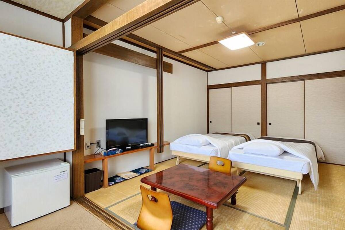 Une chambre d’hôtel avec deux lits, une télévision, un petit bureau et un sol recouvert de tatamis, dans le style traditionnel japonais.