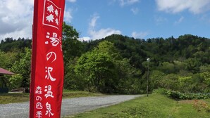A red flag with white Japanese characters, a gravel path, green trees, and a hill in the background.