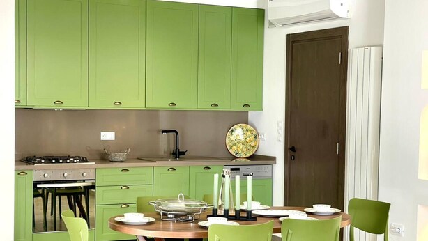 Cozinha com armários verdes, fogão e mesa de jantar para quatro pessoas.