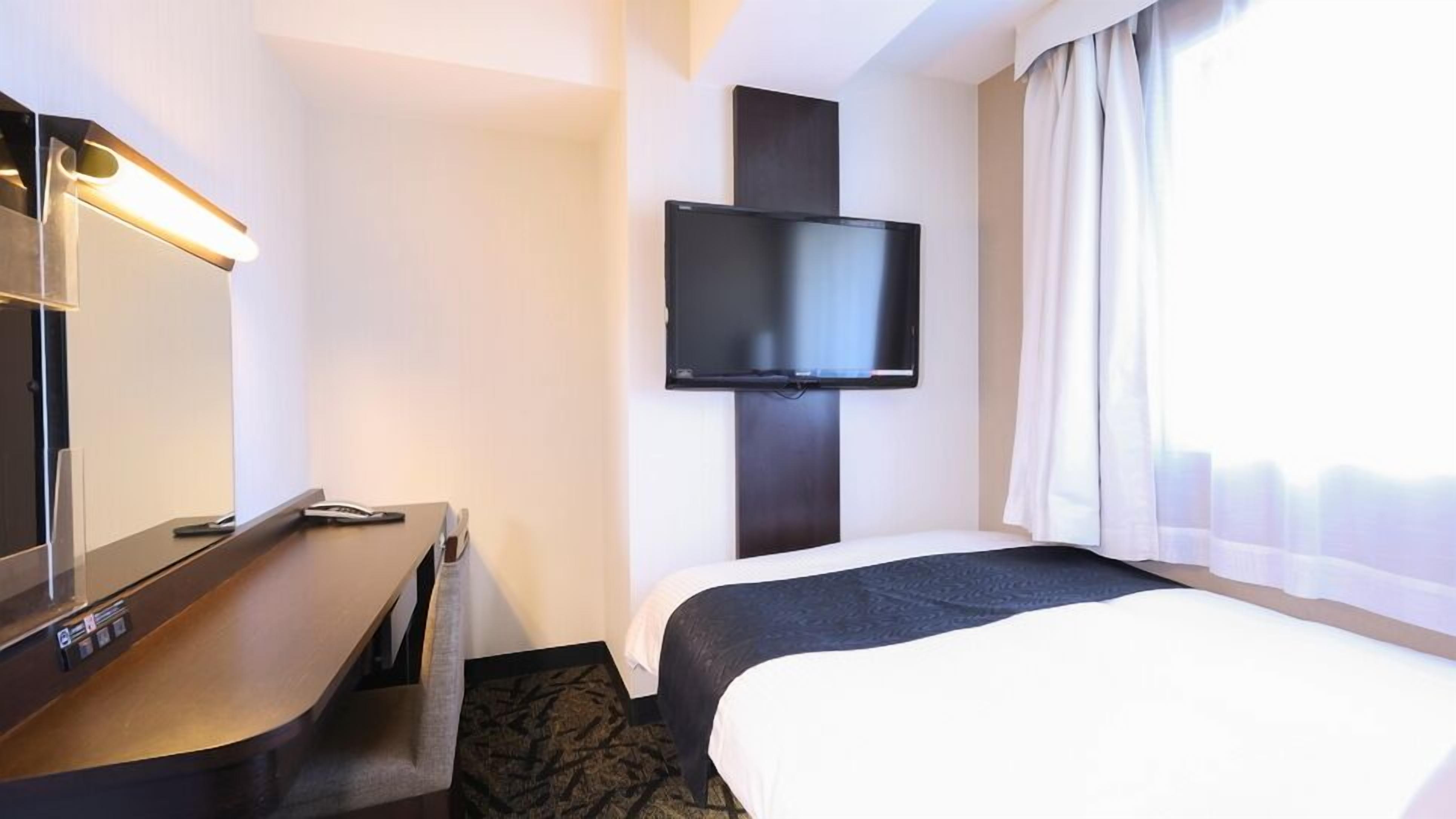 Camera d'albergo con un letto, una scrivania, una TV a schermo piatto montata a parete e una finestra con tende.