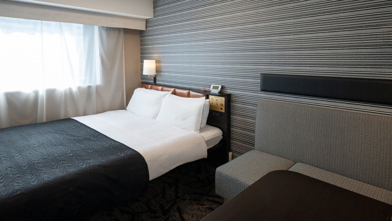 Una camera d'hotel con un letto, un comodino, una lampada e vista sull'esterno.