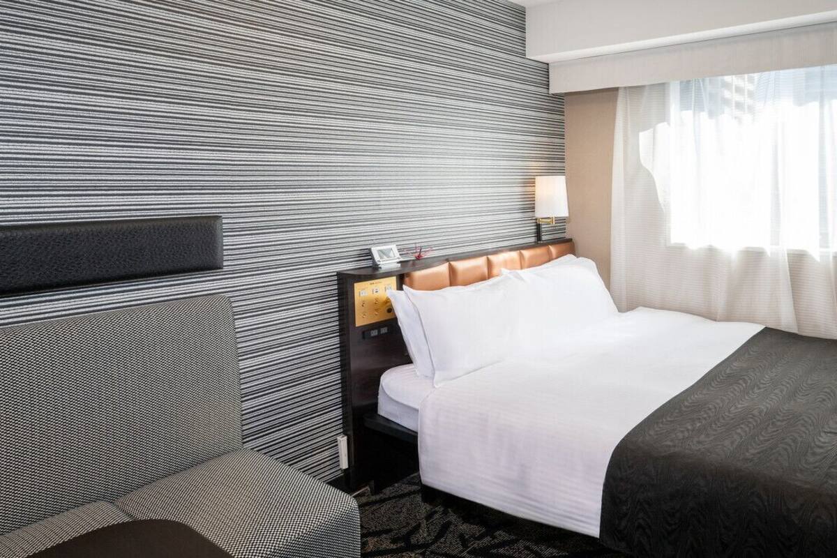 A hotel room with a bed, a nightstand, a wall clock, and a window with curtains.