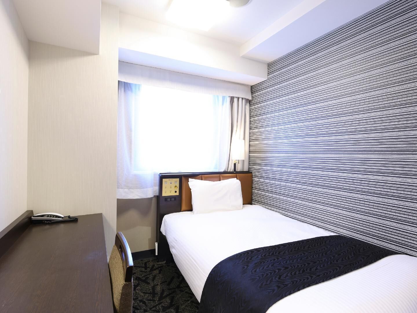 Una camera d'hotel con un letto, una scrivania, un telefono e una finestra con tende.