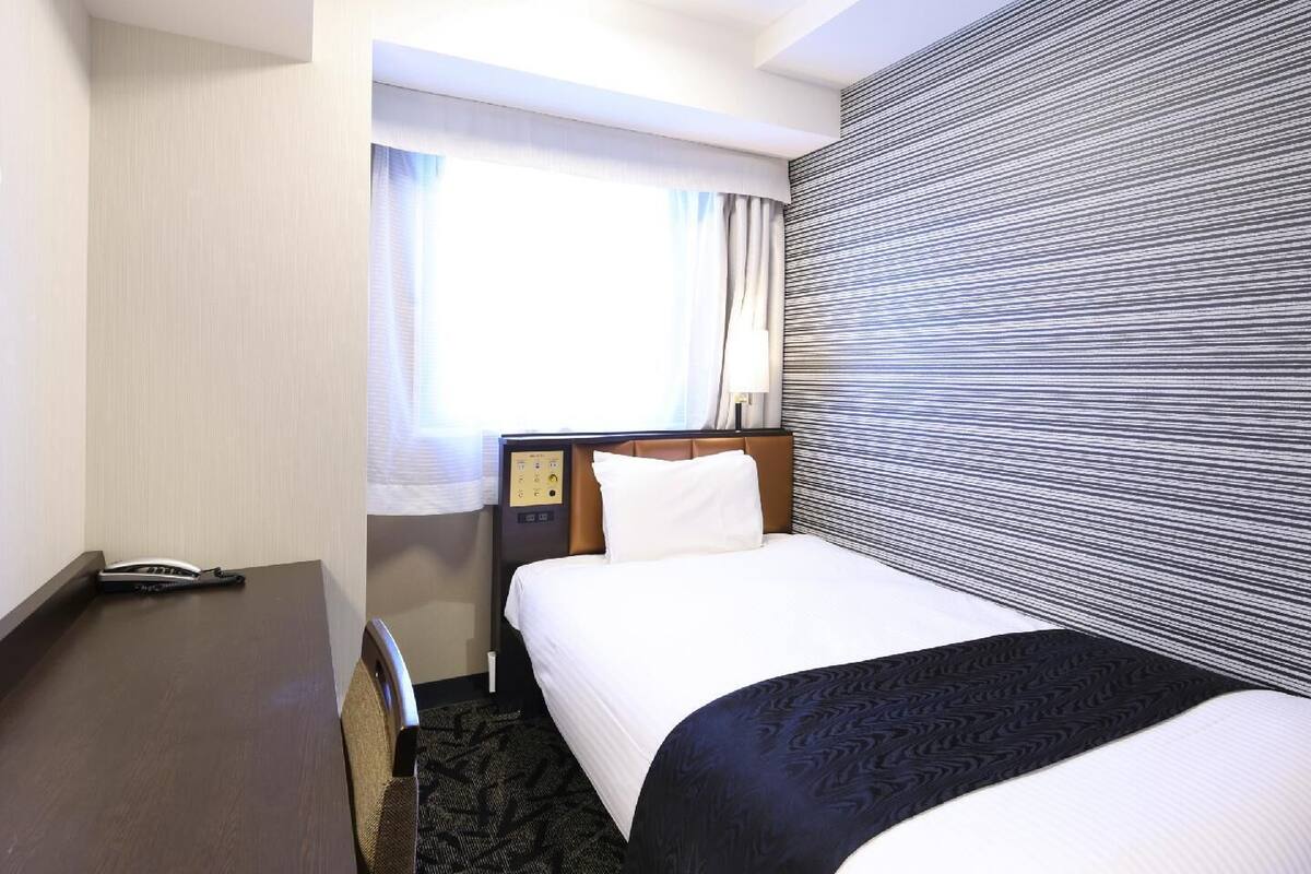 A hotel room with a bed, a desk, a telephone, and a window with curtains.