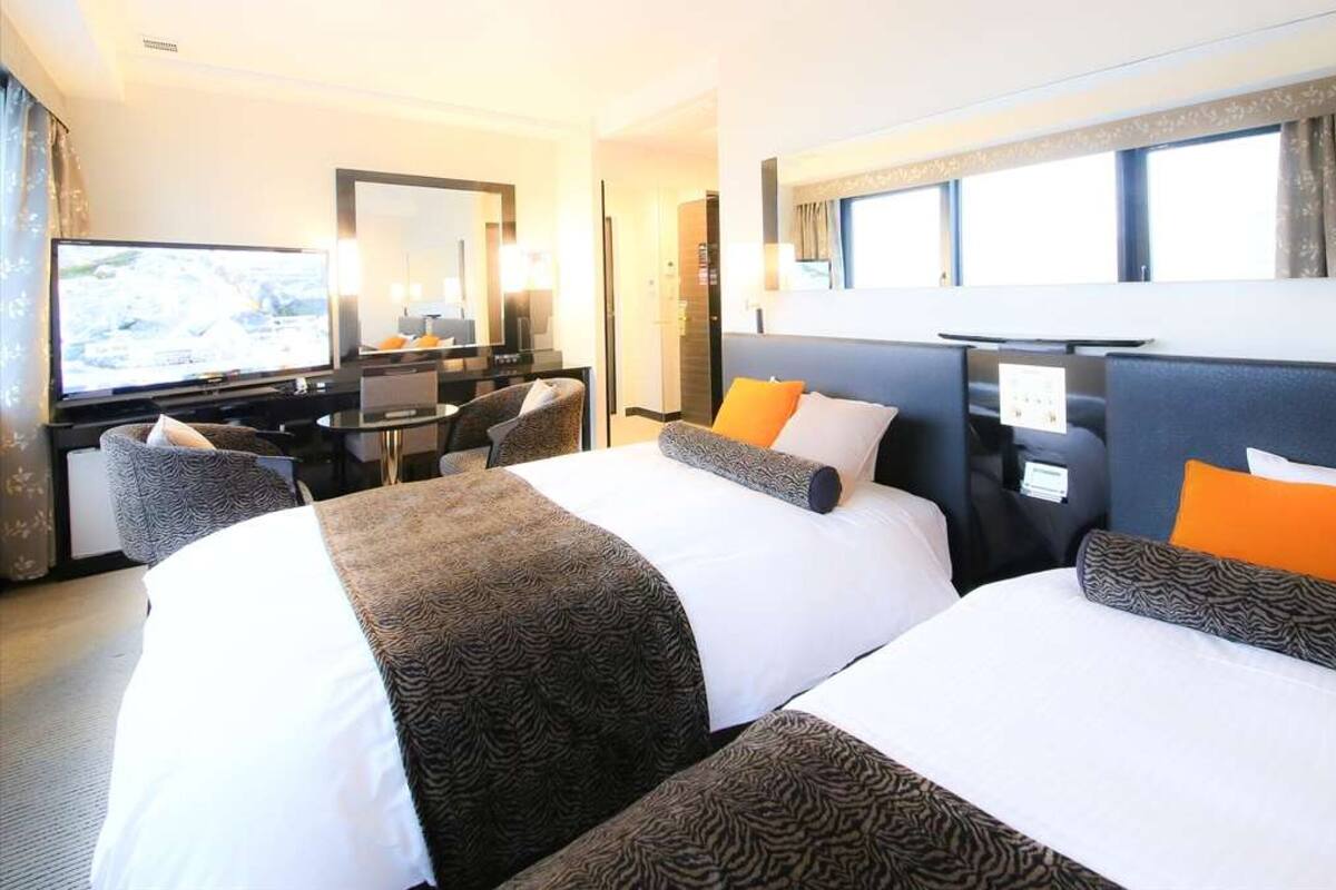 A hotel room with two beds, a desk, a television, and a window.
