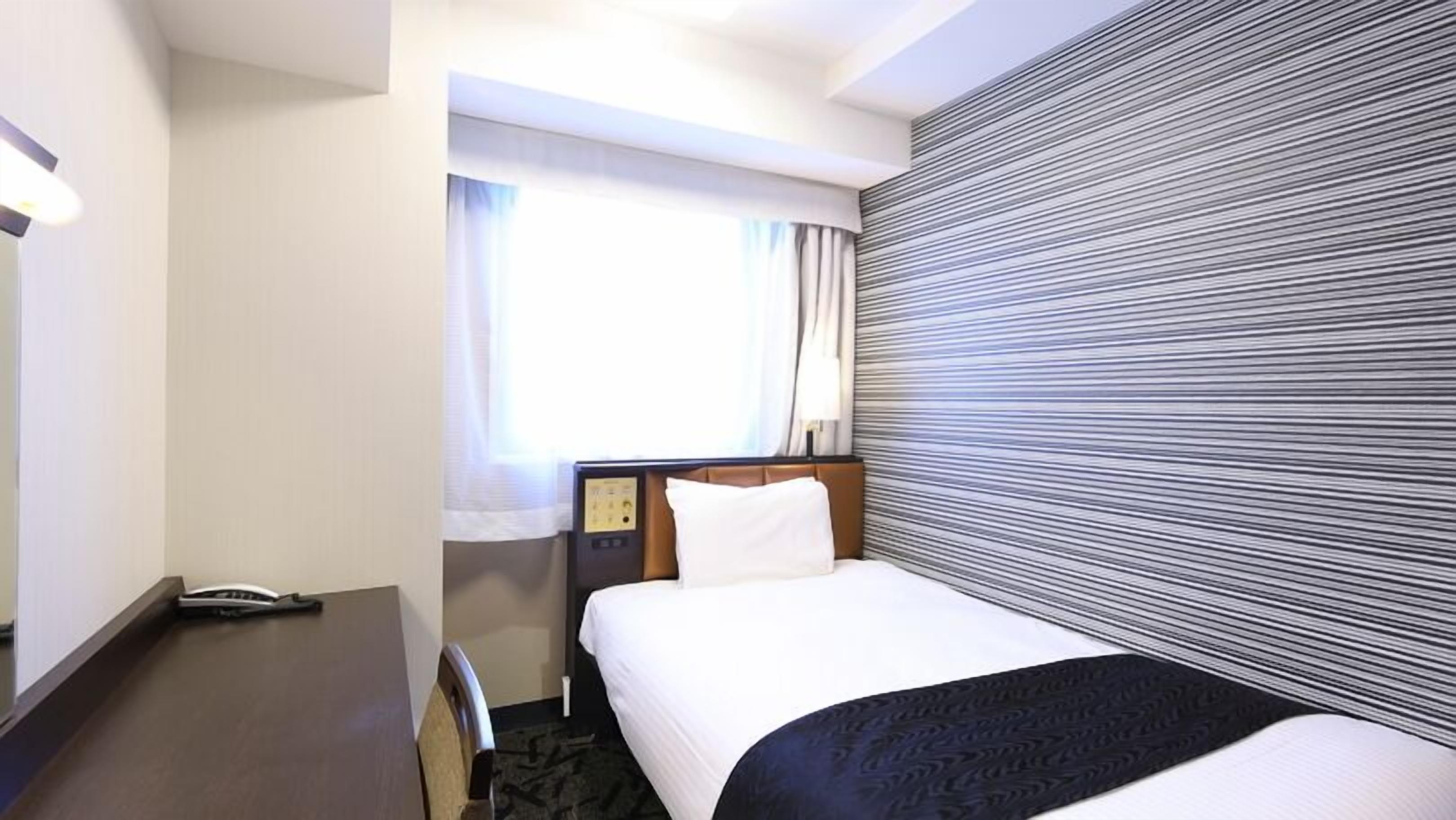 Una camera d'albergo con un letto, una scrivania, un telefono e una finestra con tende.