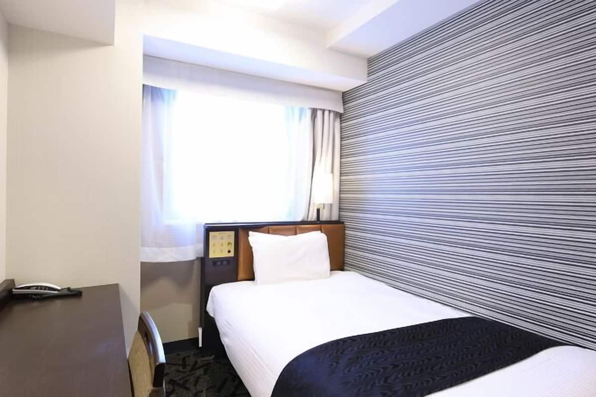 A hotel room with a bed, a desk, a telephone, and a window with curtains.