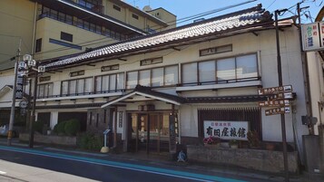 Un edificio tradicional japonés con tejado de tejas, un letrero y una pequeña entrada.