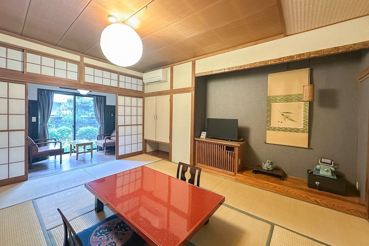 A traditional Japanese-style room with tatami flooring, a low table, and a television on a cabinet.