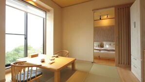 A room with a wooden dining table, chairs, a bed with a view, and a sliding door leading to another room.