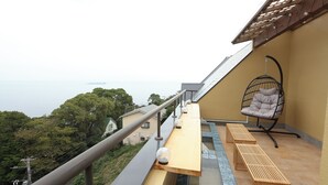 A balcony with a view of the sea, a hanging chair, and wooden benches.