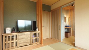 A room with a television, wooden cabinet, tatami mats, and a sliding door leading to another room.