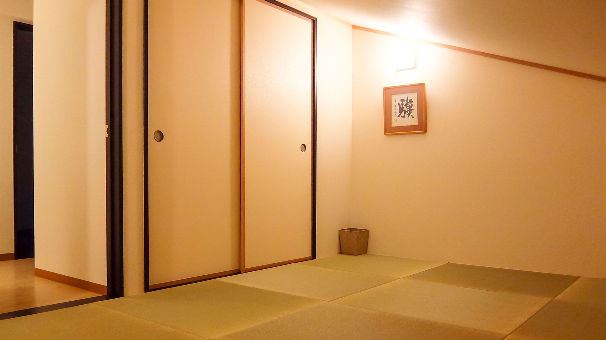 A room with tatami mats, sliding doors, and a framed calligraphy piece on the wall.
