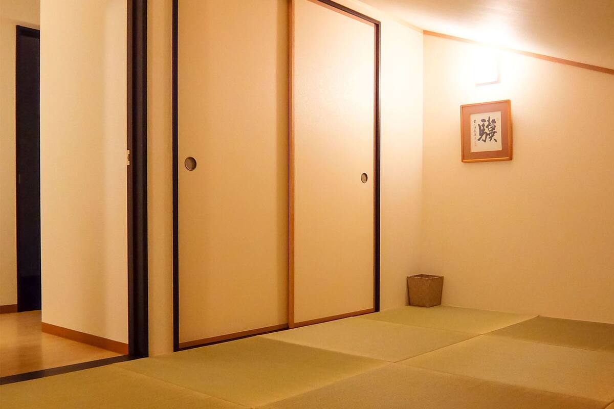A room with tatami mats, sliding doors, and a framed calligraphy piece on the wall.