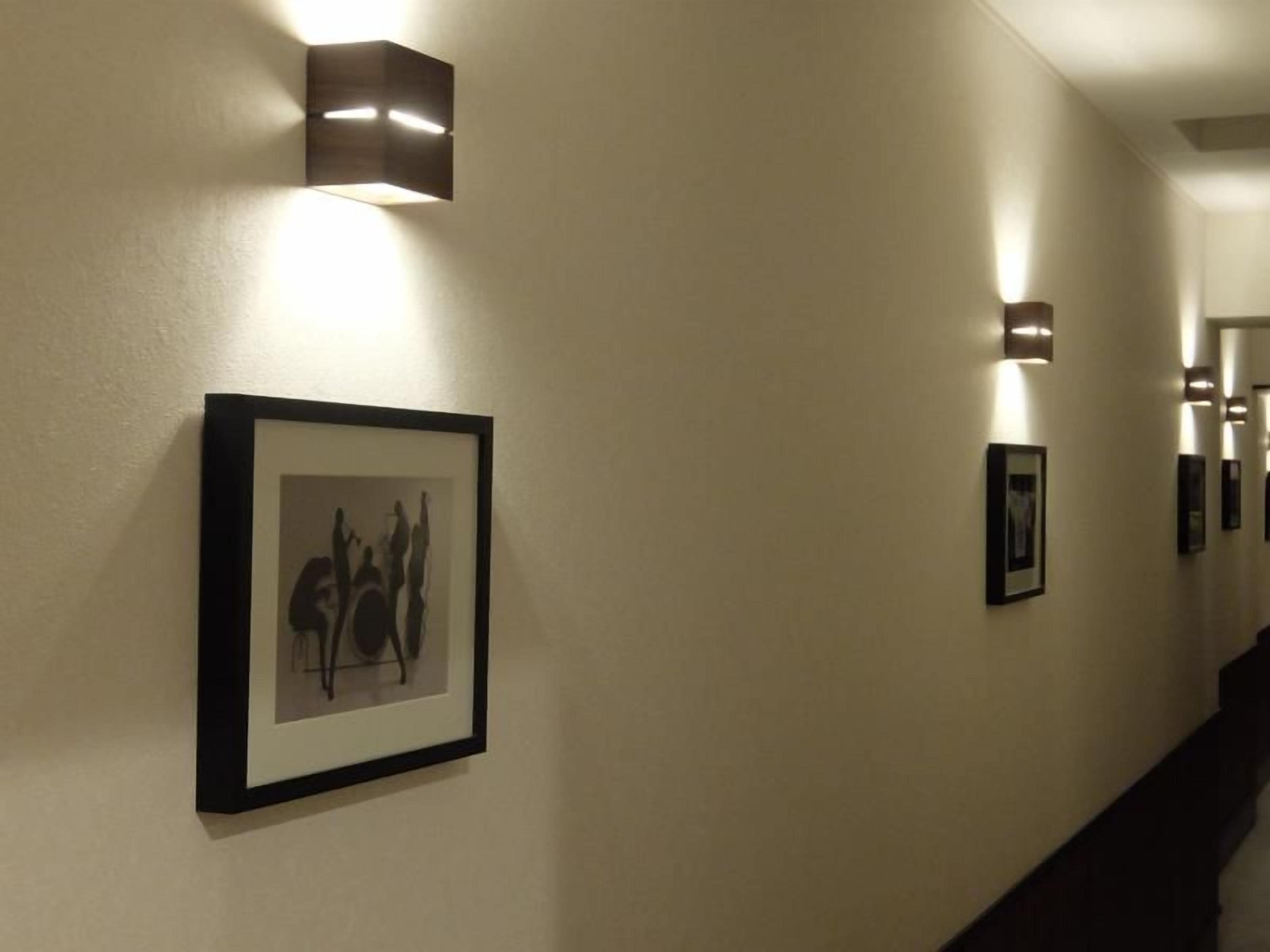 A hallway with framed artwork on the walls and wall-mounted lighting fixtures.