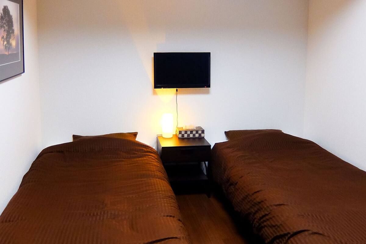 A twin room with two beds, a bedside table, a TV mounted on the wall, and a framed picture on the wall.