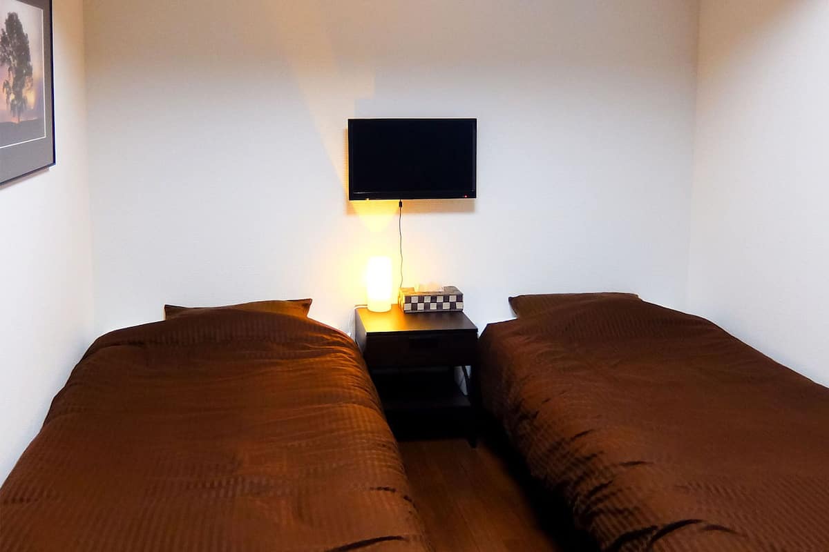 A twin room with two beds, a bedside table, a TV mounted on the wall, and a framed picture on the wall.