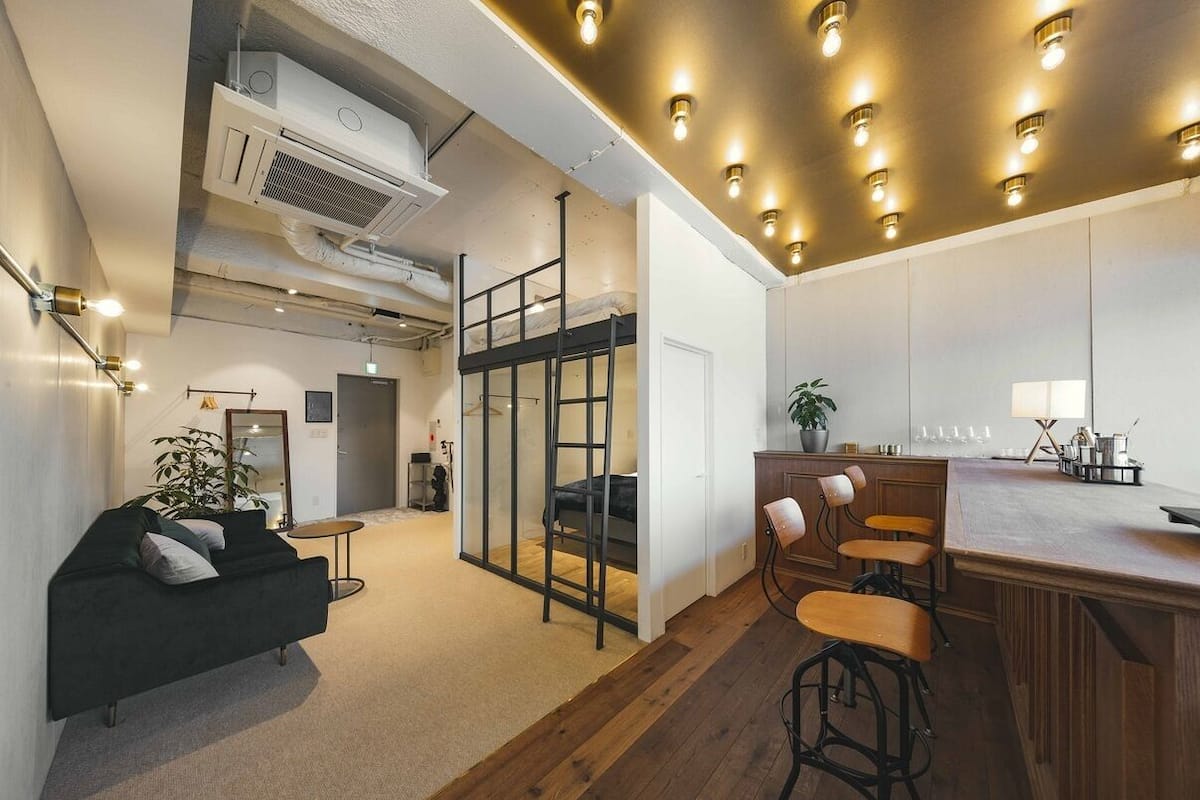 A modern interior with a bunk bed, a kitchen area, and a seating area with stools.