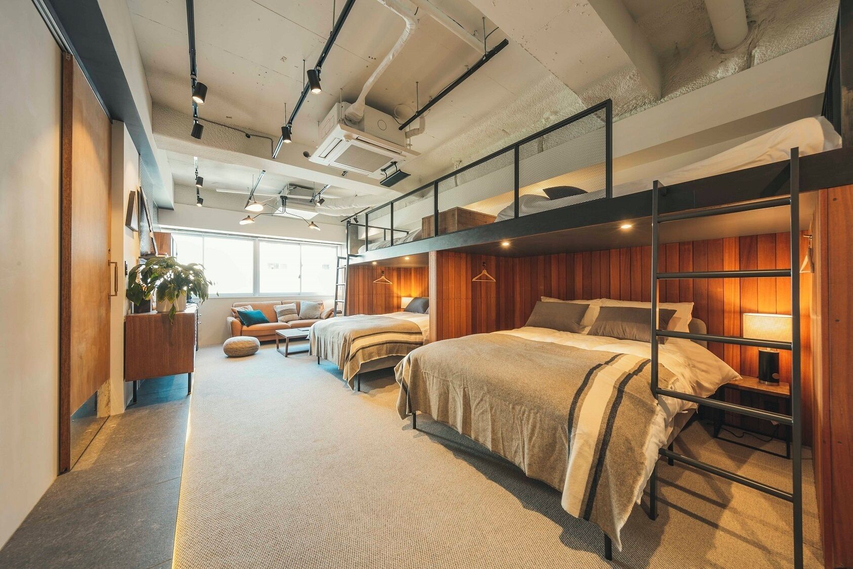 Habitación de hotel moderna con literas, sofá, escritorio y ventana grande.