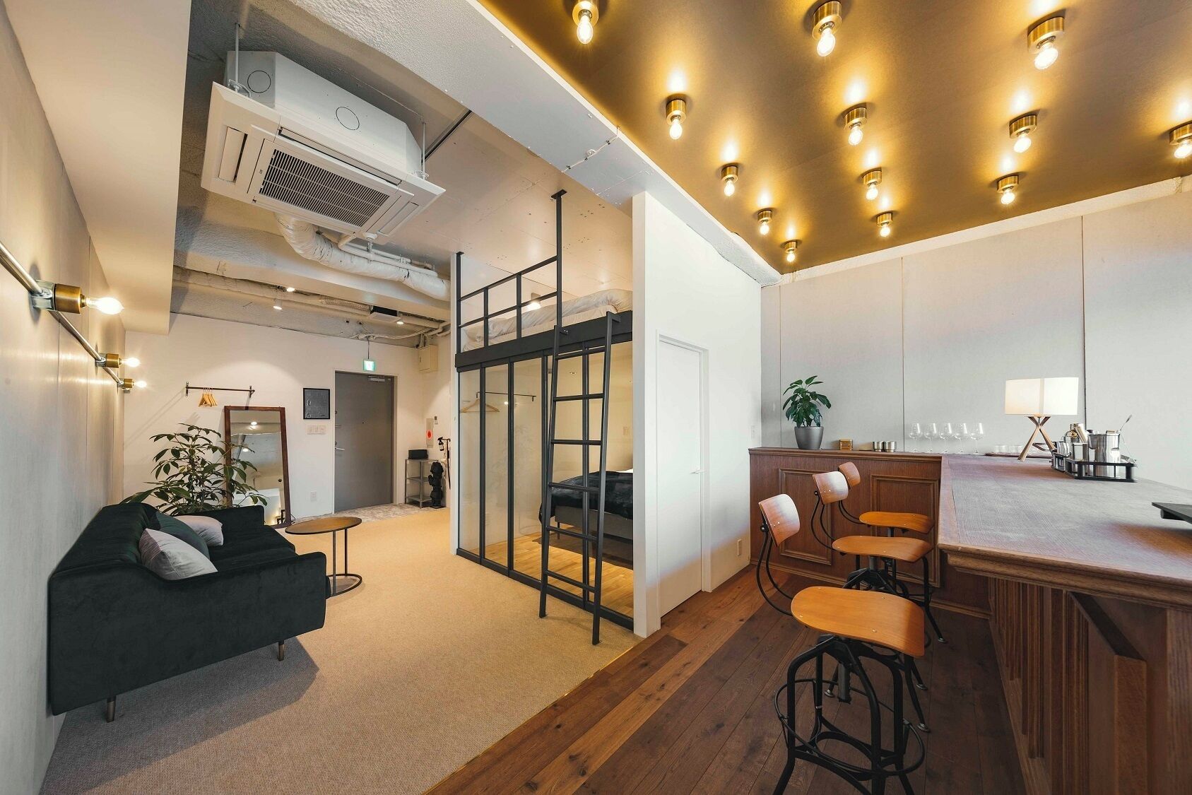 Un interior moderno con un sofá, taburetes de bar, una planta y una zona de cocina.