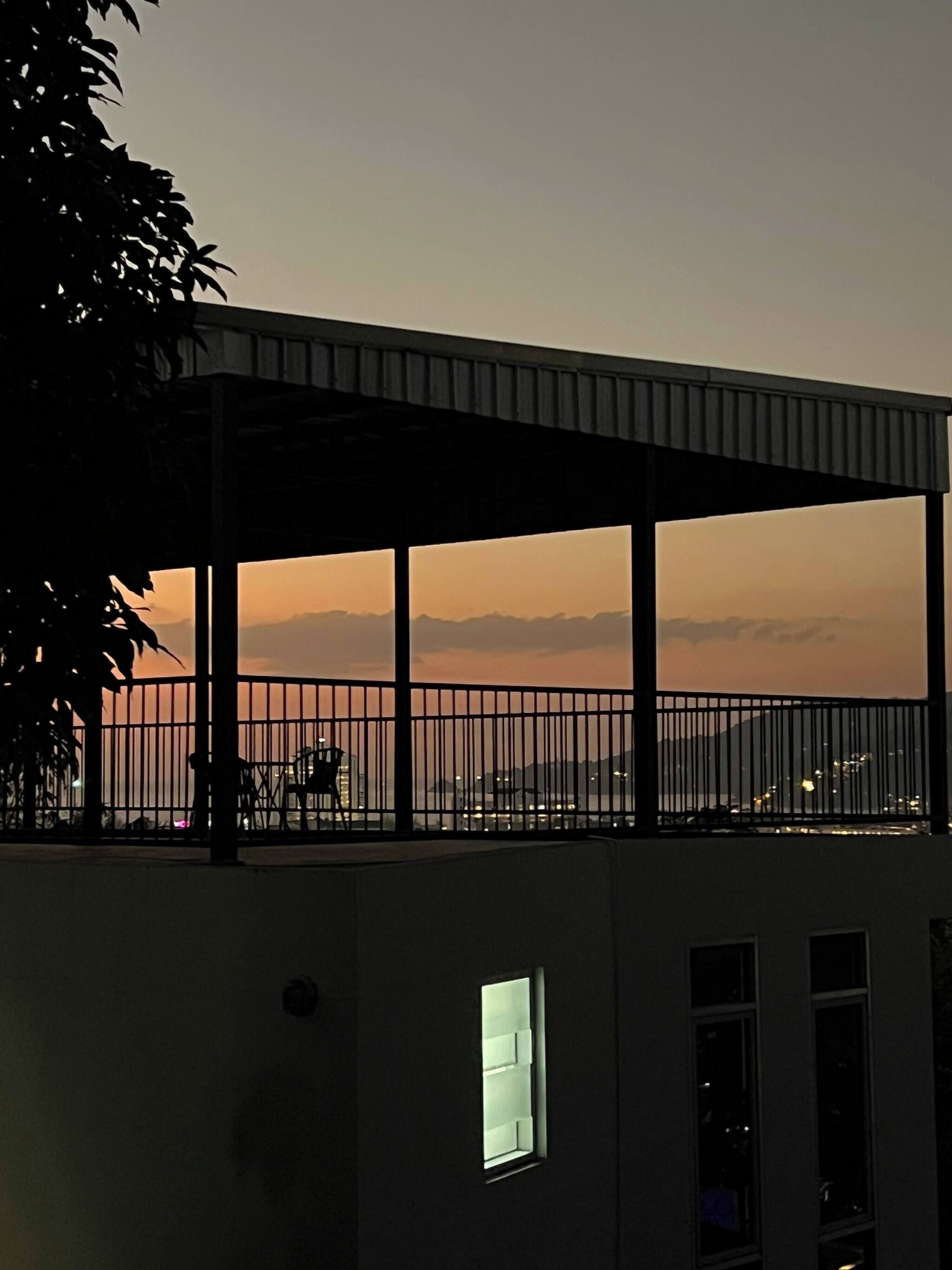 A building with a balcony overlooking a cityscape at sunset.