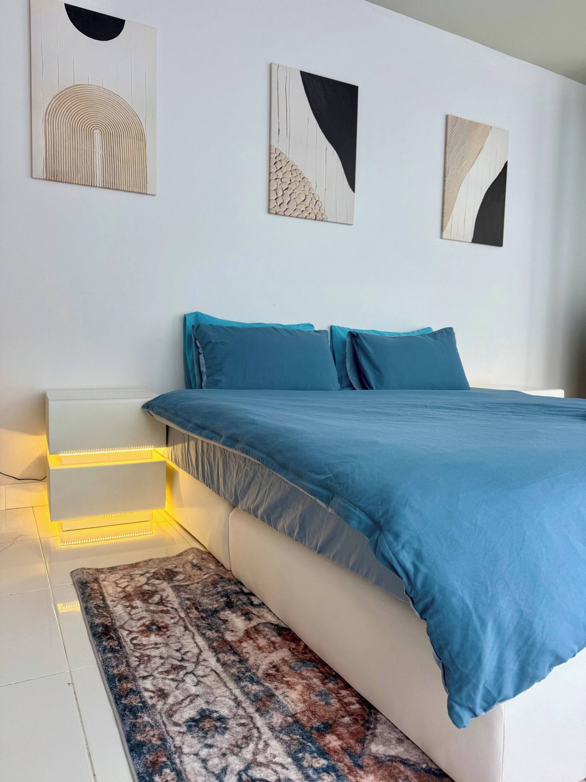 Un dormitorio moderno con cama, mesitas de noche y cuadros en la pared.