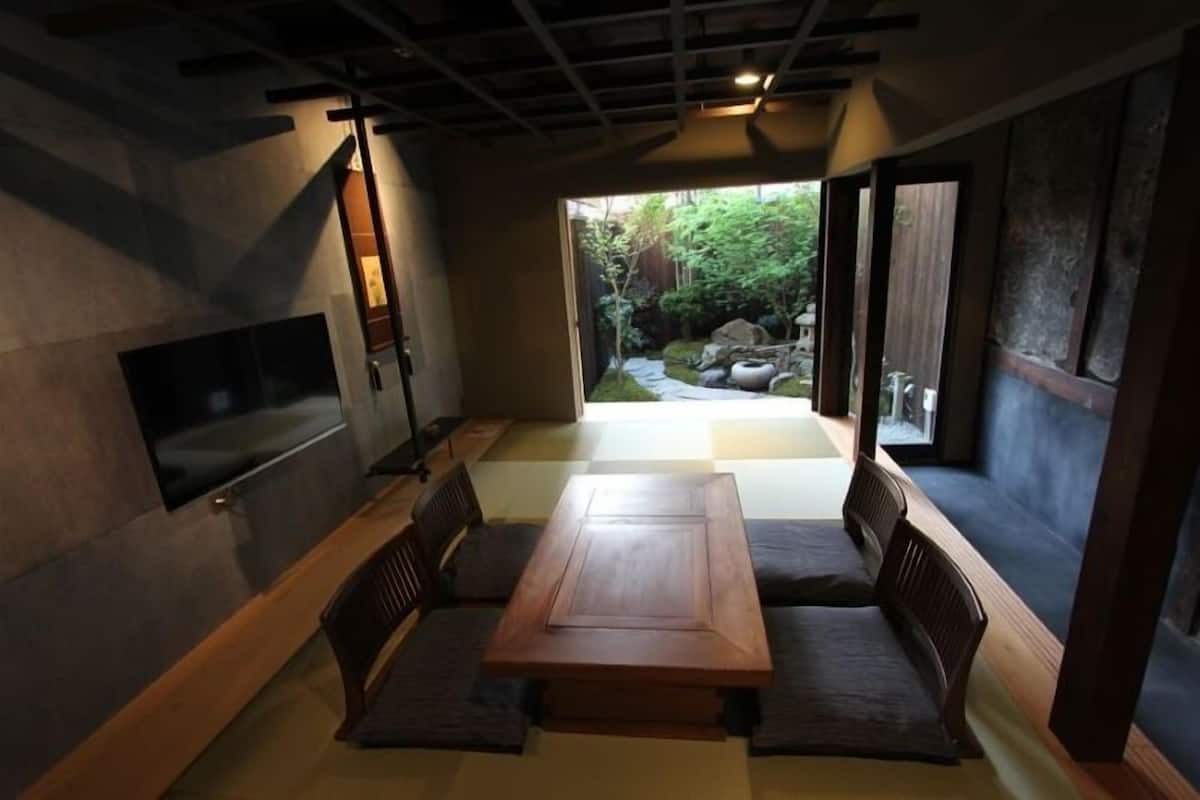 A traditional Japanese-style room with tatami flooring, a low wooden table, and a TV mounted on the wall.