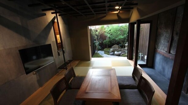 A traditional Japanese-style room with tatami flooring, a low wooden table, and a TV mounted on the wall. - Kyoto Ryoan Zen (Kyoto)