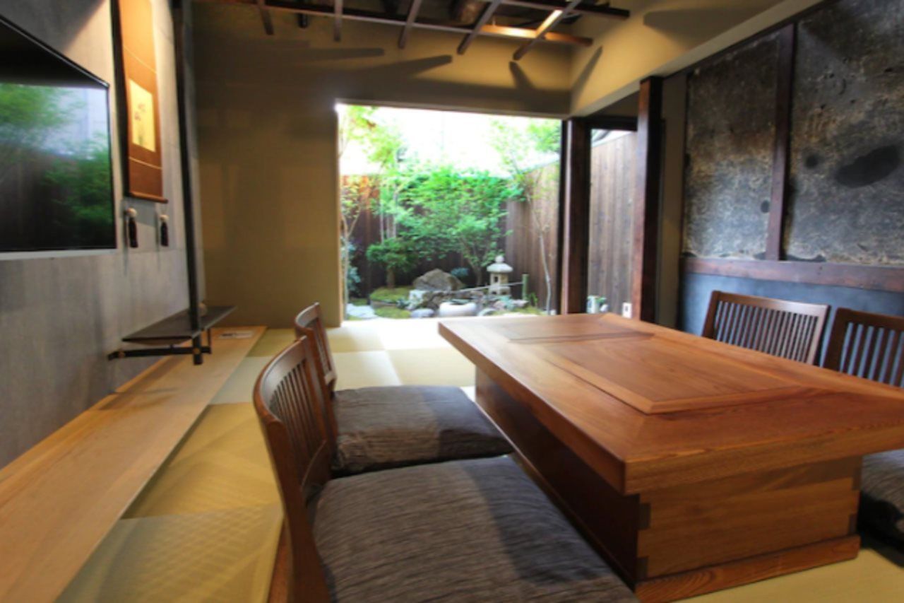 Una habitación tradicional japonesa con suelo de tatami, una mesa de madera baja y vistas a un jardín.
