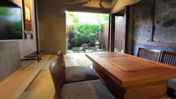 Una habitación tradicional japonesa con suelo de tatami, una mesa de madera baja y vistas a un jardín.