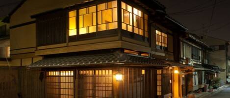 Un edificio tradicional japonés con fachada de madera y numerosas ventanas, probablemente una vivienda o pequeño local comercial.
