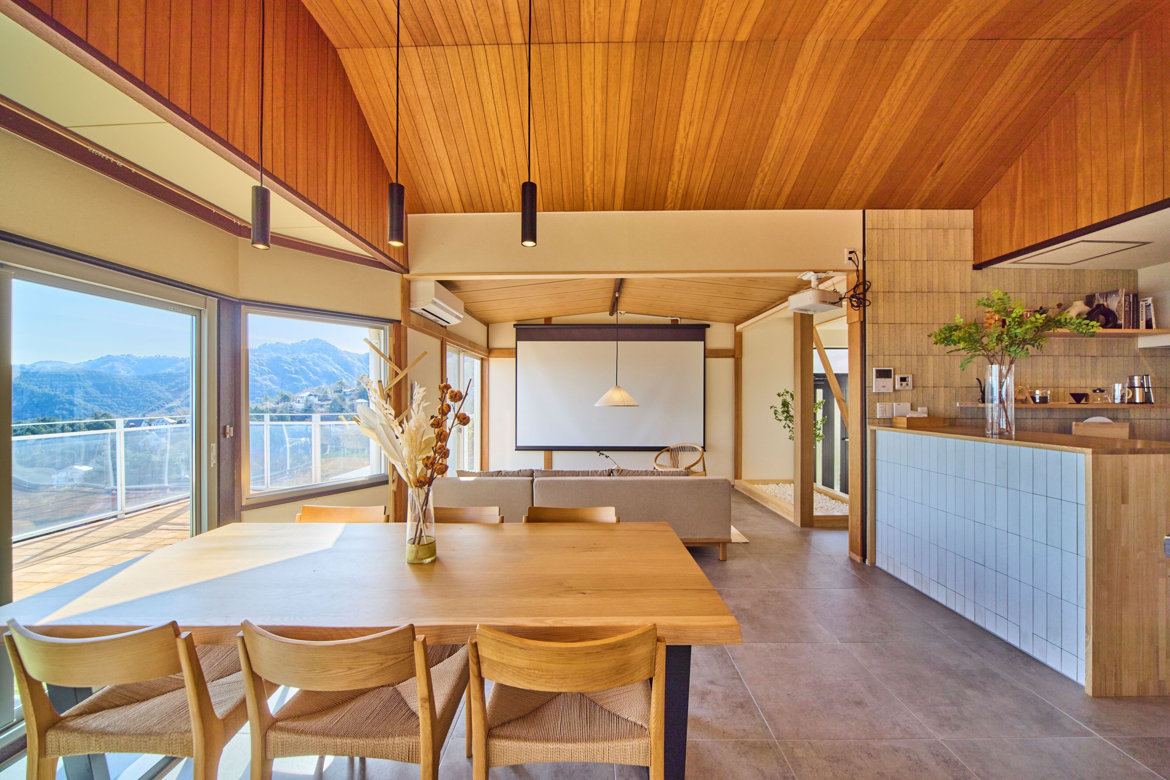 A modern kitchen with a dining area, large windows, and a view of mountains.