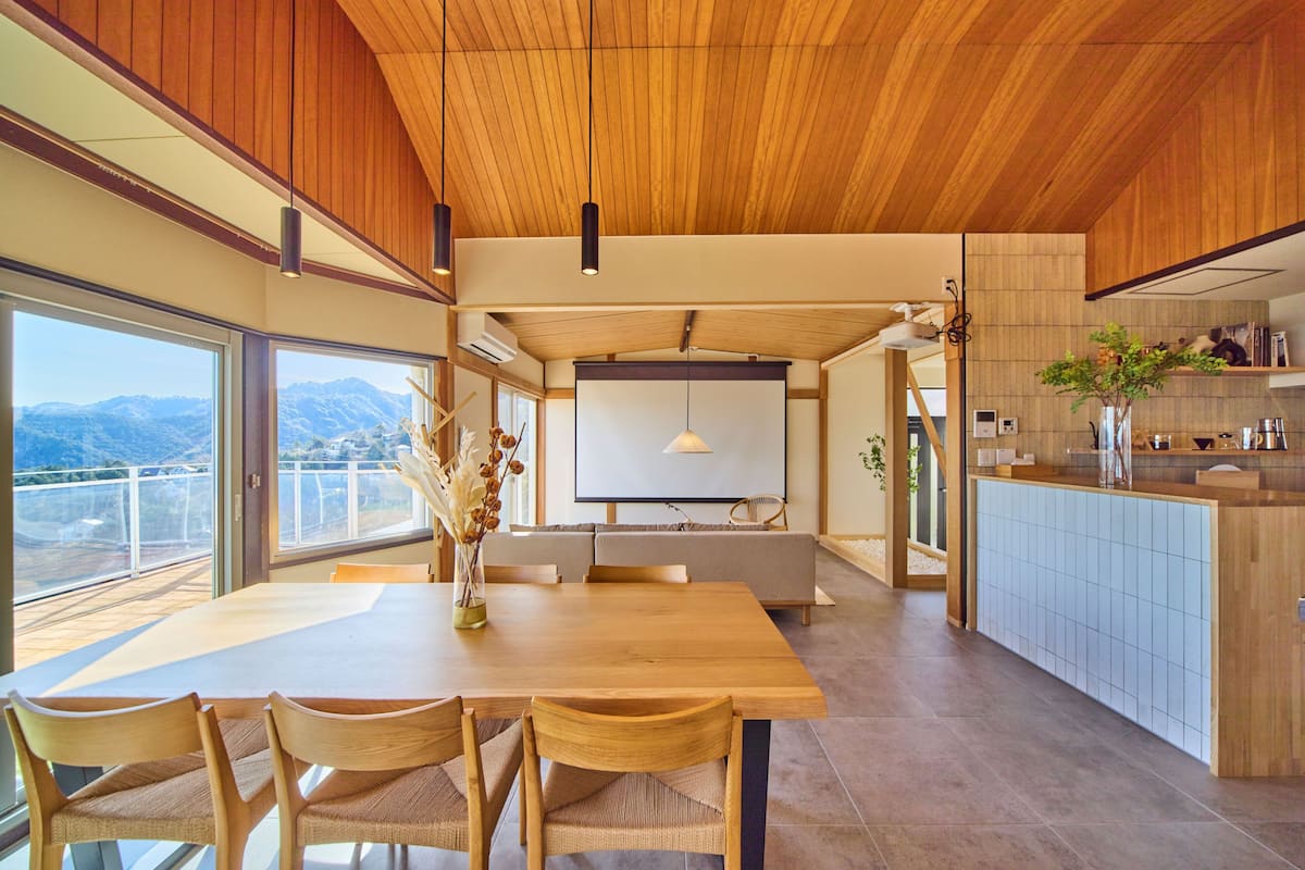 A modern kitchen with a dining area, large windows, and a view of mountains.