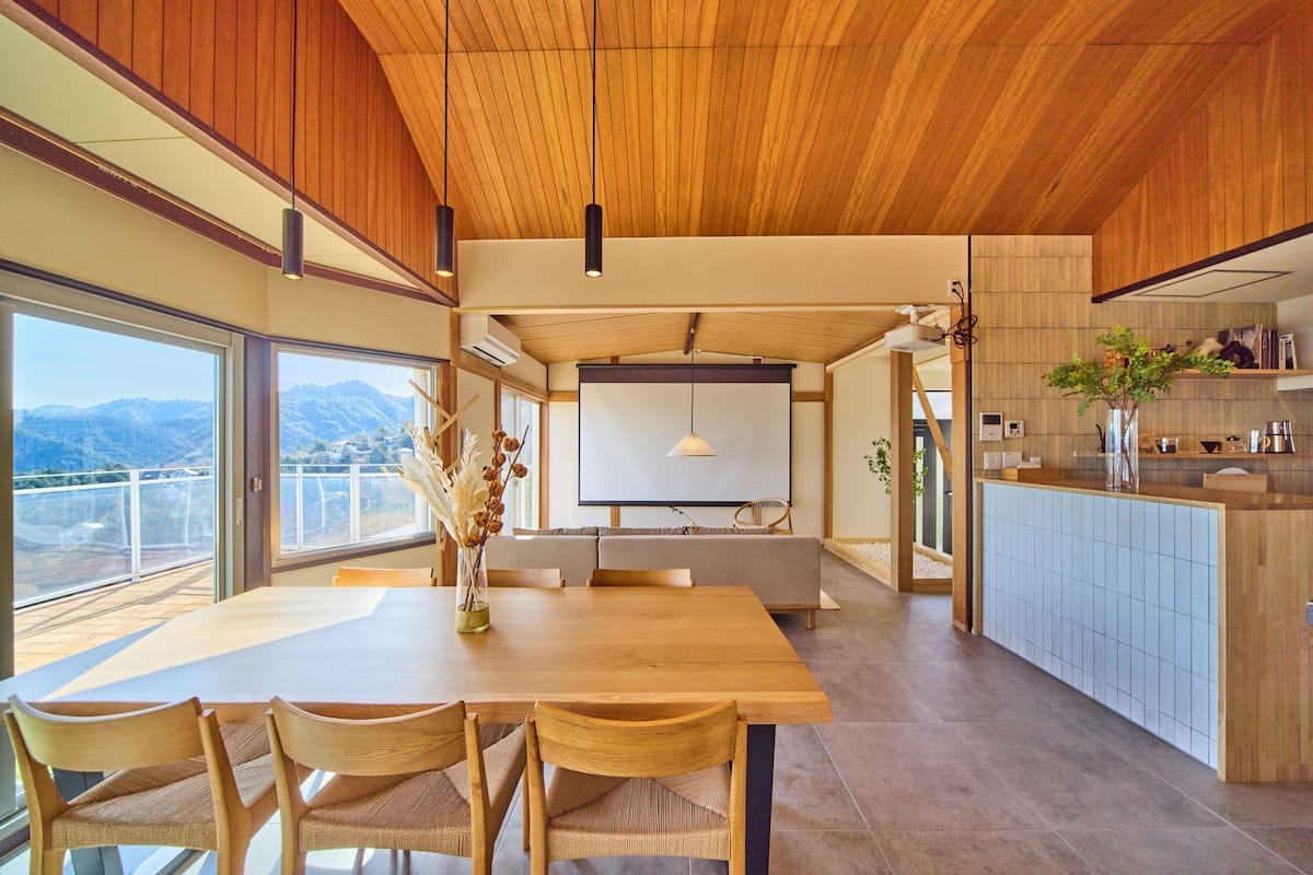 A modern kitchen with a dining area, wooden ceiling, and large windows overlooking a mountainous landscape.