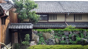 A traditional Japanese building with a tiled roof, wooden structure, and a stone wall with greenery. - Demizu Machiya (Kyoto)