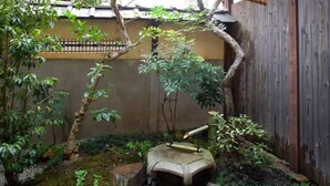 A garden with a stone fountain, a wooden fence, and various plants. - Demizu Machiya (Kyoto)