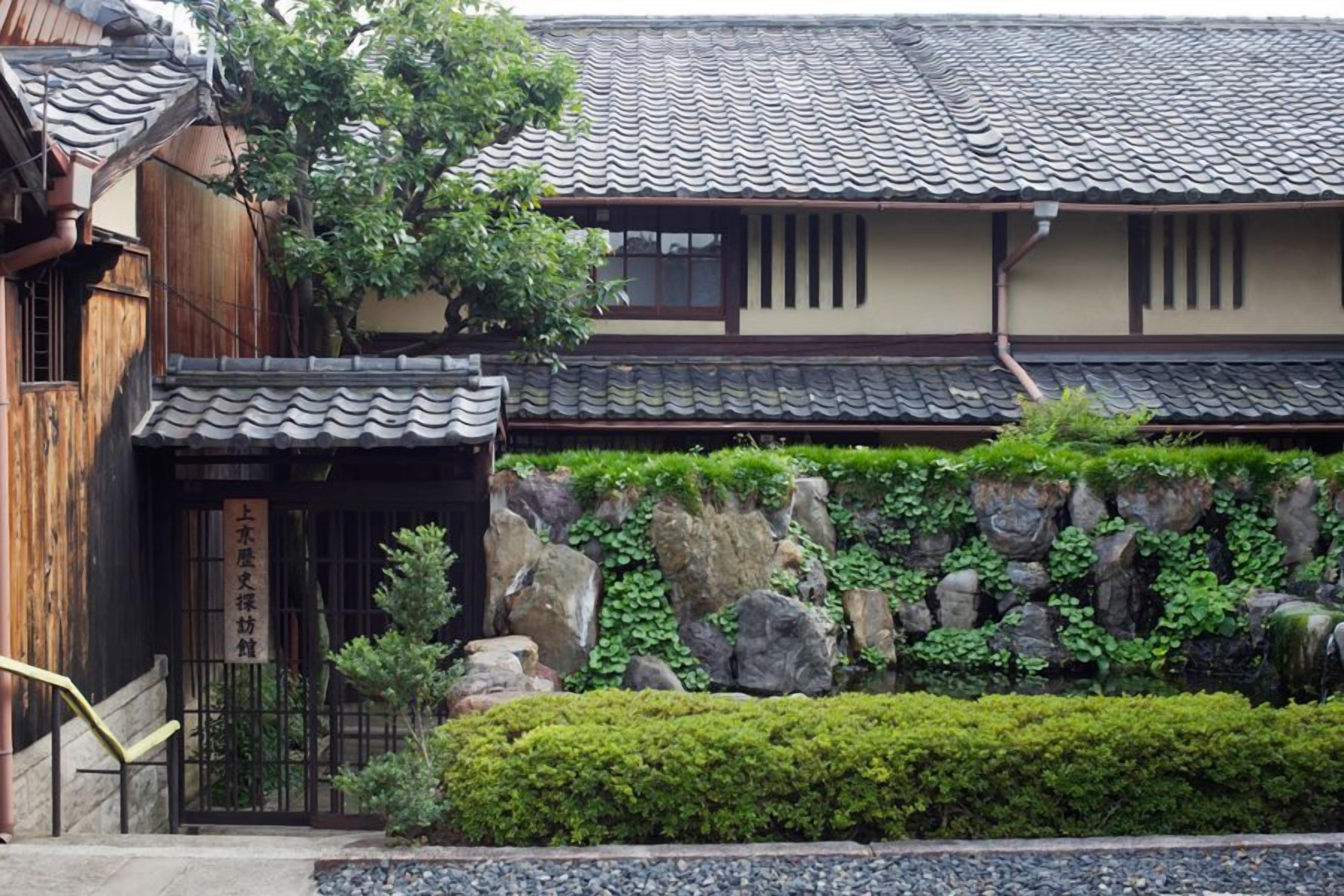 Un bâtiment japonais traditionnel, doté d’un toit en tuiles, d’une structure en bois et d’un mur de pierre orné de verdure.