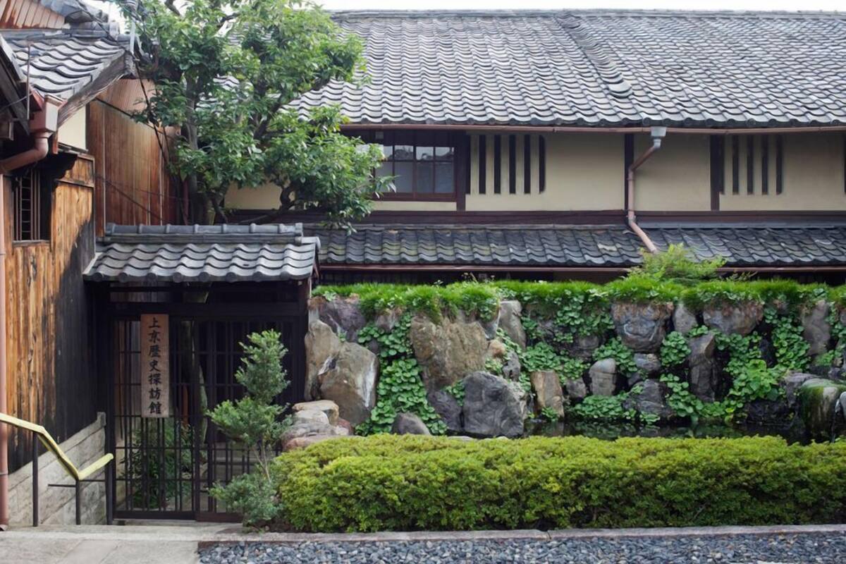 Un edificio japonés tradicional con tejado de tejas, estructura de madera y pared de piedra con vegetación.