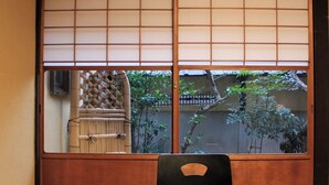 A traditional Japanese room with tatami flooring, a sliding shoji screen, and a view of a bamboo fence and trees. - Demizu Machiya (Kyoto)