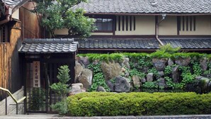 A traditional Japanese building with a tiled roof, a stone wall with greenery, and a wooden entrance. - Demizu Machiya (Kyoto)