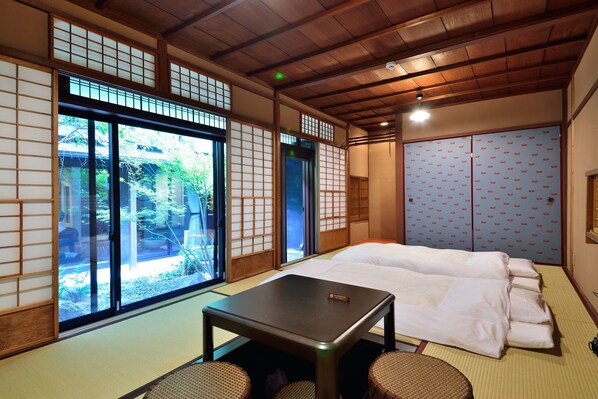 A traditional Japanese-style room with tatami flooring, a bed with white bedding, a small table, and sliding doors with a pattern. - Takeya Kitano Honkan (Kyoto)