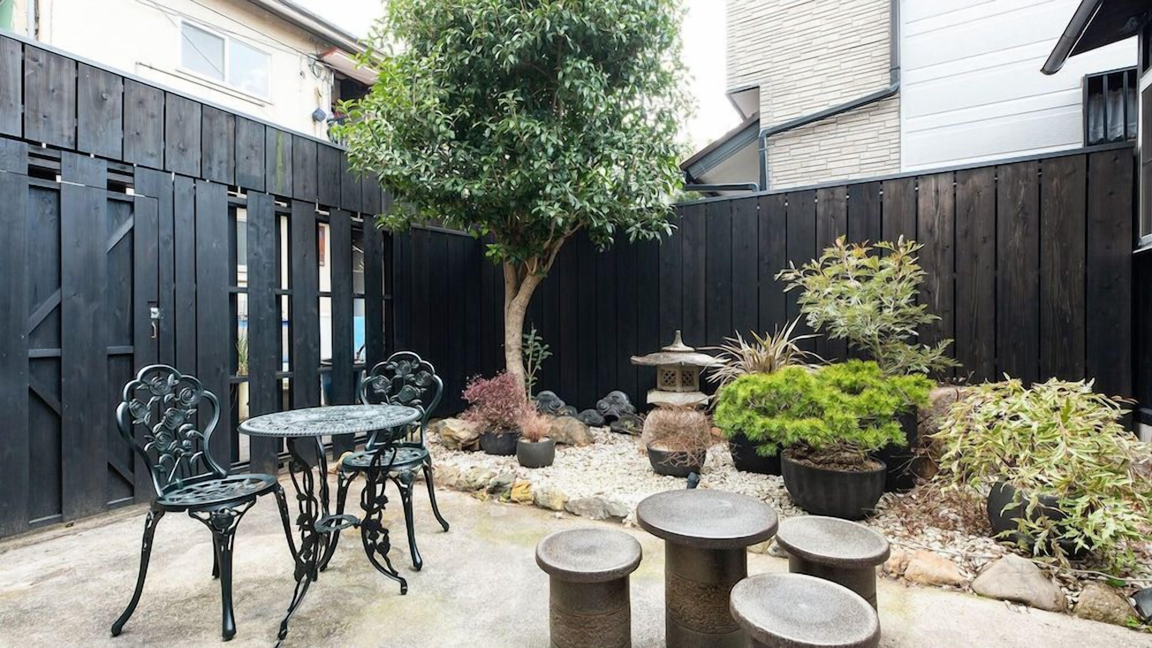 A patio area with a round table and chairs, surrounded by potted plants and a decorative stone feature.
