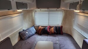Un interior de autocaravana acogedor, con un sofá modular, una mesa y una ventana con persianas.